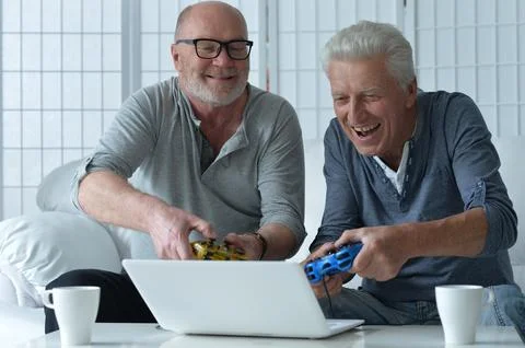 Two old men sitting at table and playing video game Stock Photos