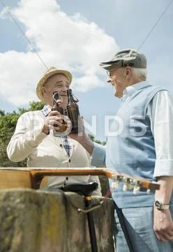 Two Old Men Toasting With Beer Bottles In The Park