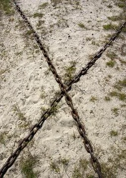 Two old rusty iron chains form X pattern to sand 写真素材