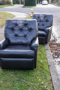 Two old, torn, abandoned leather lounge chairs on a grass strip by a street  Stock Photos