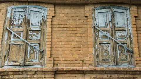 Two old windows closed with blue shutters with peeling paint on a vintage hou Stock Photos