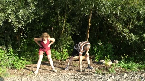 Two older adults actively exercise outdoors: a man works with dumbbells while Stock Footage 341854283