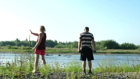 Two older adults exercise beside a river: a man performs strength exercises w Stock Footage 341854739
