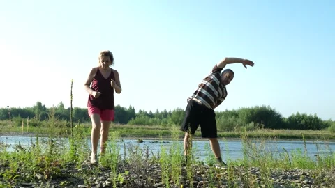 Two older adults exercise outdoors as a man performs a side bend while a woma Stock Footage 341854530