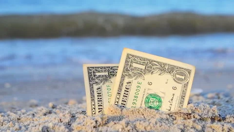 Two one dollar bills half buried in sand on sandy seashore close-up. 库存影片 167108583