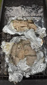 Two open aluminum foil packets revealing roasted pork meat and onions cooking 库存照片