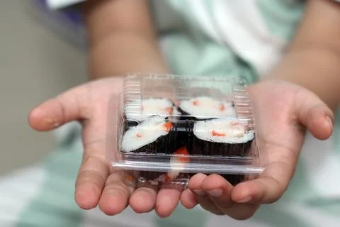 Two open hands holding a clear plastic takeaway box filled with small nori-.. Stock Photos