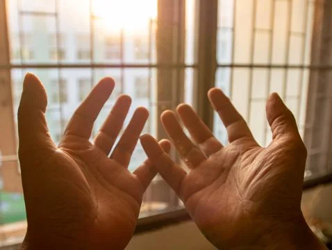Two open hands palms facing up raised toward sunlight through window with w.. Stock Photos