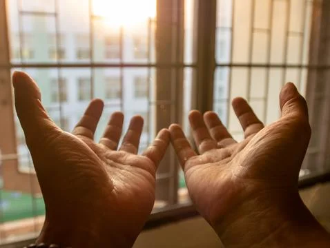 Two open hands palms facing up raised toward sunlight through window with w.. Stock Photos