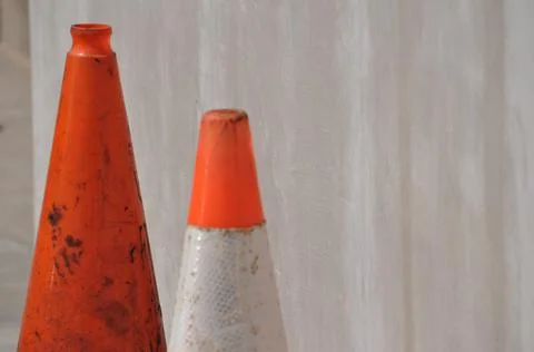 Two orange and white caution cones against light brown concrete background Foto stock