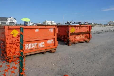 Two orange dumpsters at construction site on a wet sandy beach  Stock Photos