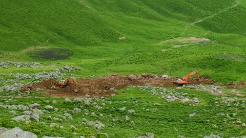 Two orange excavators digs ground on the green hill. Resort construction site Stock Footage 254938309