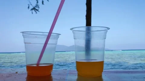 Two orange juice drinks in plastic cups by the beach Stock Footage 243431331