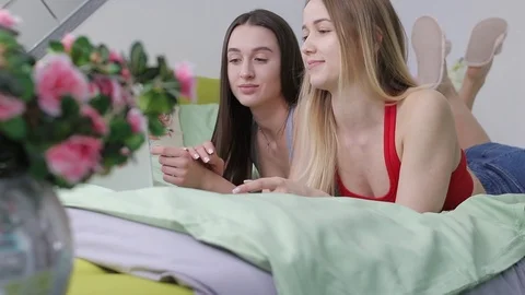 Two ordinary girls lying on the bed and choose the goods in the online store Stock Footage 107820997