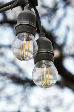 Two outdoor string lights hanging on a wire, showcasing warm LED filaments Foto stock