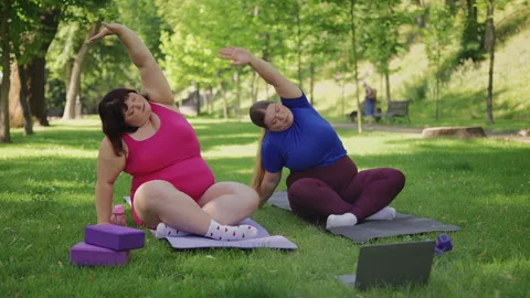 Two overweight sisters doing side body stretches in park during video tutorial 스톡 동영상 333634201
