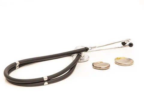 TWO PACEMAKER BATTERIES SURROUNDED BY A STETHOSCOPE WHITE BACKGROUND Stock Photos
