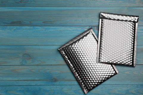 Two padded envelopes with bubble wrap on light blue wooden background, flat l Stock Photos