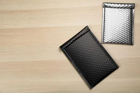 Two padded envelopes with bubble wrap on wooden background, flat lay. Space f Stock Photos