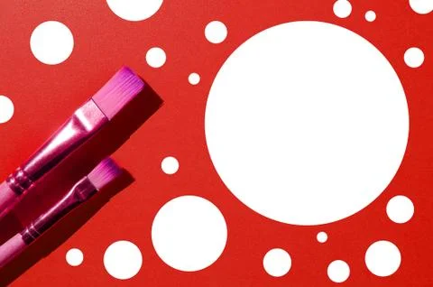 Two paint brushes of different sizes next to white circle on an red backgroun Foto stock