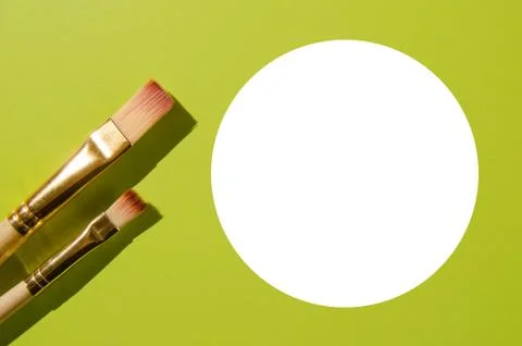 Two paint brushes of different sizes next to white circle on an olive backgro Stock Photos