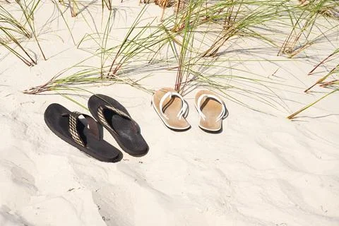Two pair of flip-flops on a sandy beach, with grass growing in the background Stock Photos