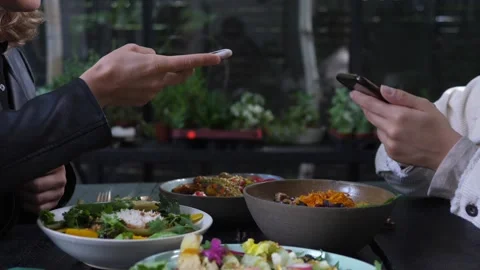 Two pair of hands taking pictures of healthy vegan meals served on black wooden Video stock 139008042