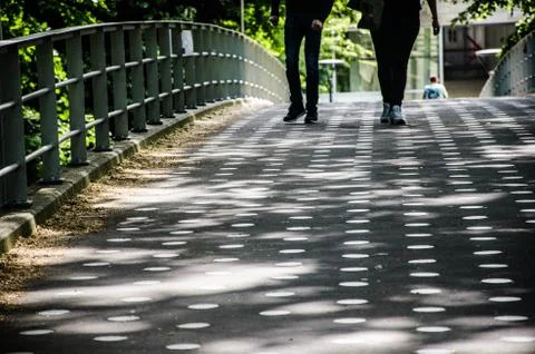 Two pair of legs walking over a bridge with sunlight making a pettern with sh Stock Photos