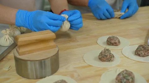 Two pairs of chefs' hands in gloves make khinkali on the table. Video stock 250398682