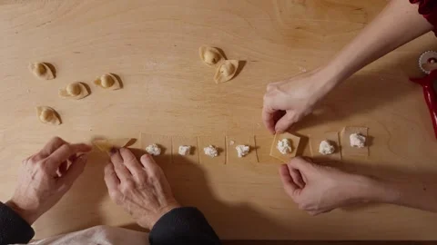 Two Pairs of Hands Folding Pasta Squares on Wooden Surface During Homemade Stock Footage 327298746