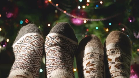 Two pairs of legs in warm woolen socks next to a beautiful Christmas tree Stock Footage 102876504