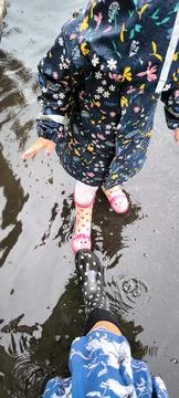 Two pairs of rubber boots in a puddle: the joy of rain, two generations Stock Photos