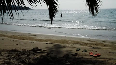 Two pairs of slippers on beach sand and woman in beautiful ocean in Island Stock Footage