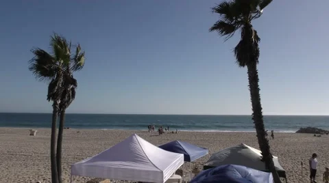 Two palm trees and tens on beach blowing in the wind with waves cashing on sh Stock Footage 67617422