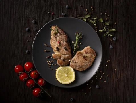 Two pan-seared pork chops rest on a dark gray plate Stock Photos