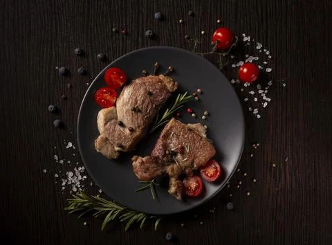 Two pan-seared pork chops rest on a dark gray plate Stock Photos