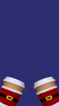 Two paper beige cups with white lid dressed in santa claus clothes on blue .. Stock Photos