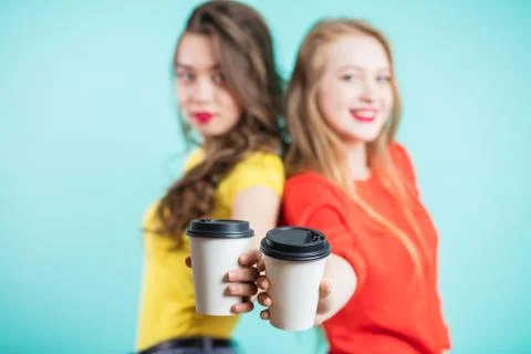Two paper cups of coffee in the foreground, in focus. Young girls holding han Stock Photos