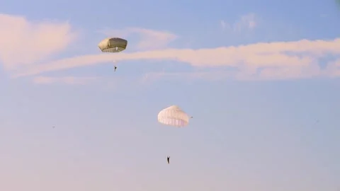 Two parachutists drift down through a light cloud cover, one under a white Stock Footage 286345620