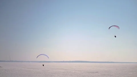 Two paraglider soaring above the ground covered with snow against the blue sky Stock Footage 73966273