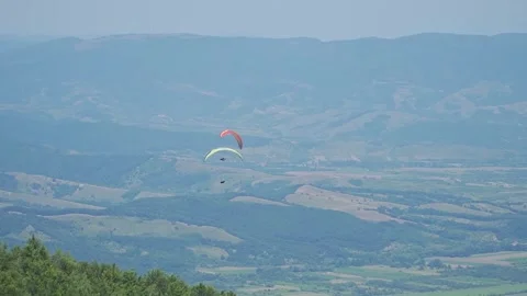 Two Paragliders Cross Paths Above Forest and Mountains Stock Footage 304561774