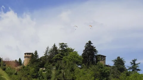Two Paragliders Flying Over an Ancient Castle and Trees Against a Cloudy Sky Stock Footage 243940864