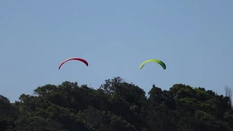 Two paragliders gracefully soar through a clear blue sky, a vibrant red and.. Vídeo Stock 332833199