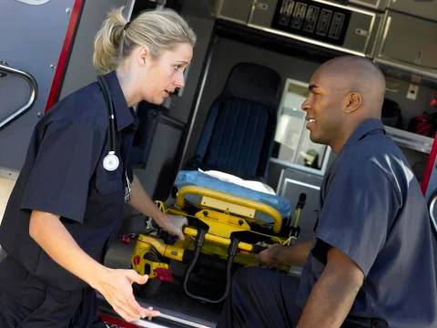 Two paramedics cheerfully removing empty gurney from ambulance Stock Photos