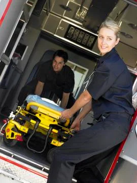 Two paramedics cheerfully removing empty gurney from ambulance Stock Photos
