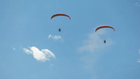 Two paramotor pilots operate powered paragliders with orange canopies, soaring 스톡 동영상 318201358