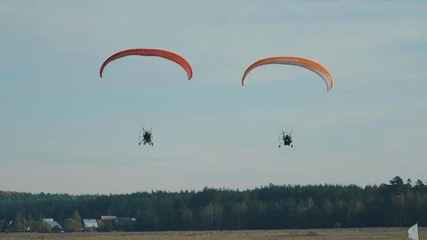 Two paratrikes fly to the camera over an autumn field on a clear and sunny day. Stock Footage 129548755