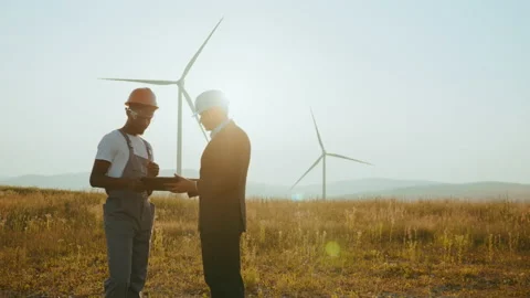 Two partners standing on field with wind turbines. Engineer and inspector Stock Footage 170642902