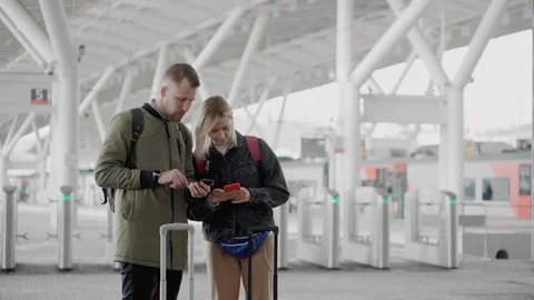Two passengers are using smartphones, standing on platform of railway station Stock Footage 108061105