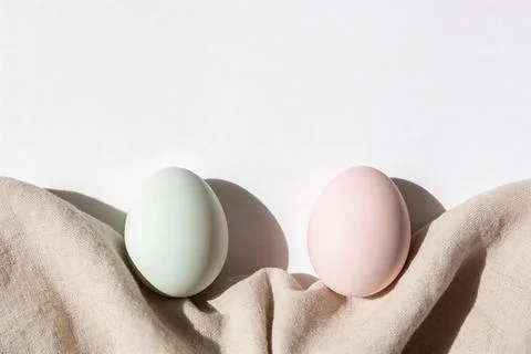 Two pastel colored eggs, one mint green and one soft pink, resting on a tex.. 스톡 사진
